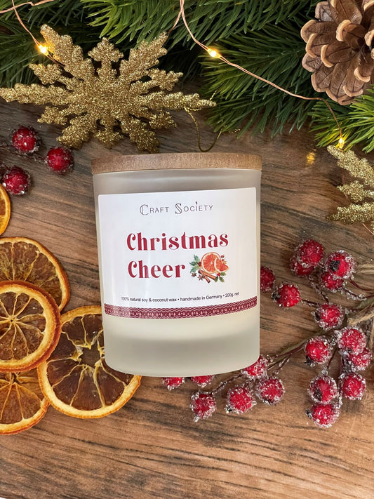 The Christmas Cheer scented candle in a frosted jar on a winter decorated background
