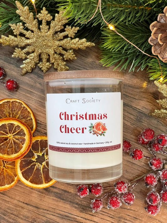 The Christmas Cheer scented candle in a clear glass jar on a winter decorated background