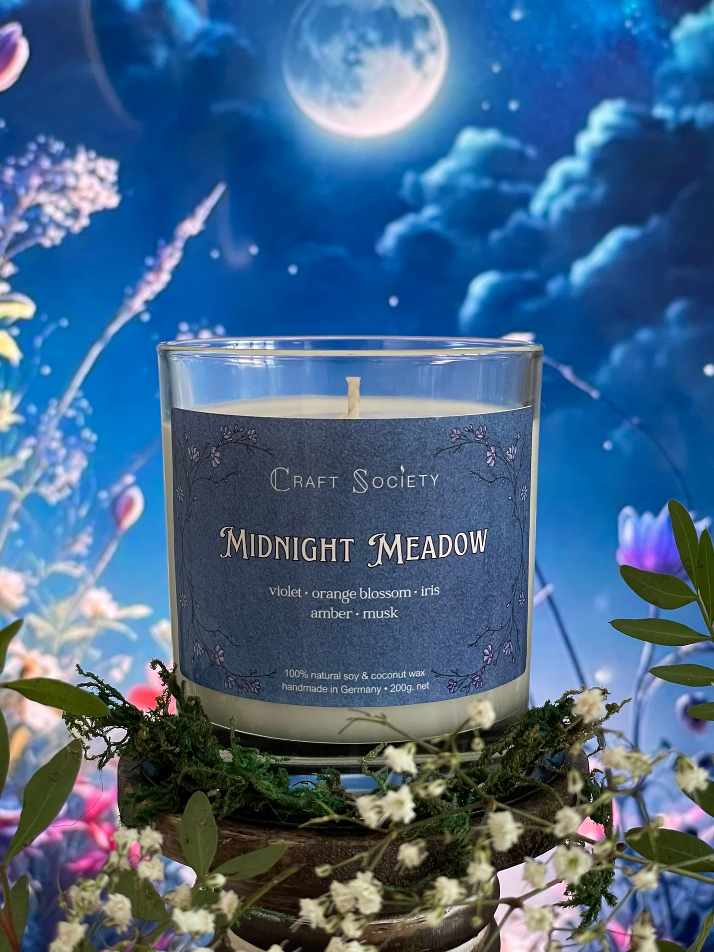 A scented candle called Midnight Meadow on a floral and night background, unlit, clear glass jar, regular version with cotton wick