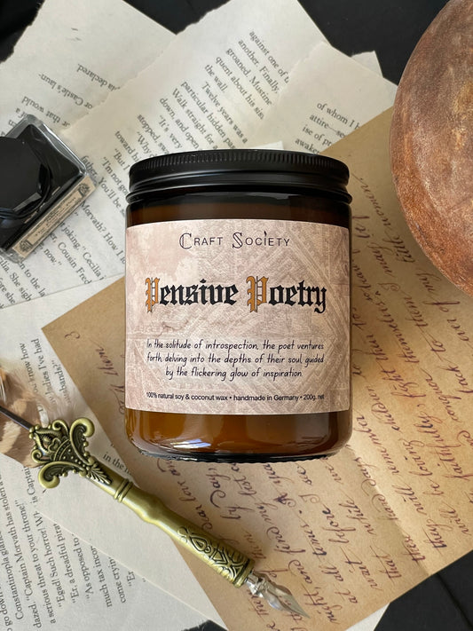The Pensive Poetry scented candle in an amber jar from above on a dark academia background