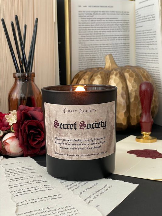 A burning deluxe scented candle, black jar, on a dark academia decorated background