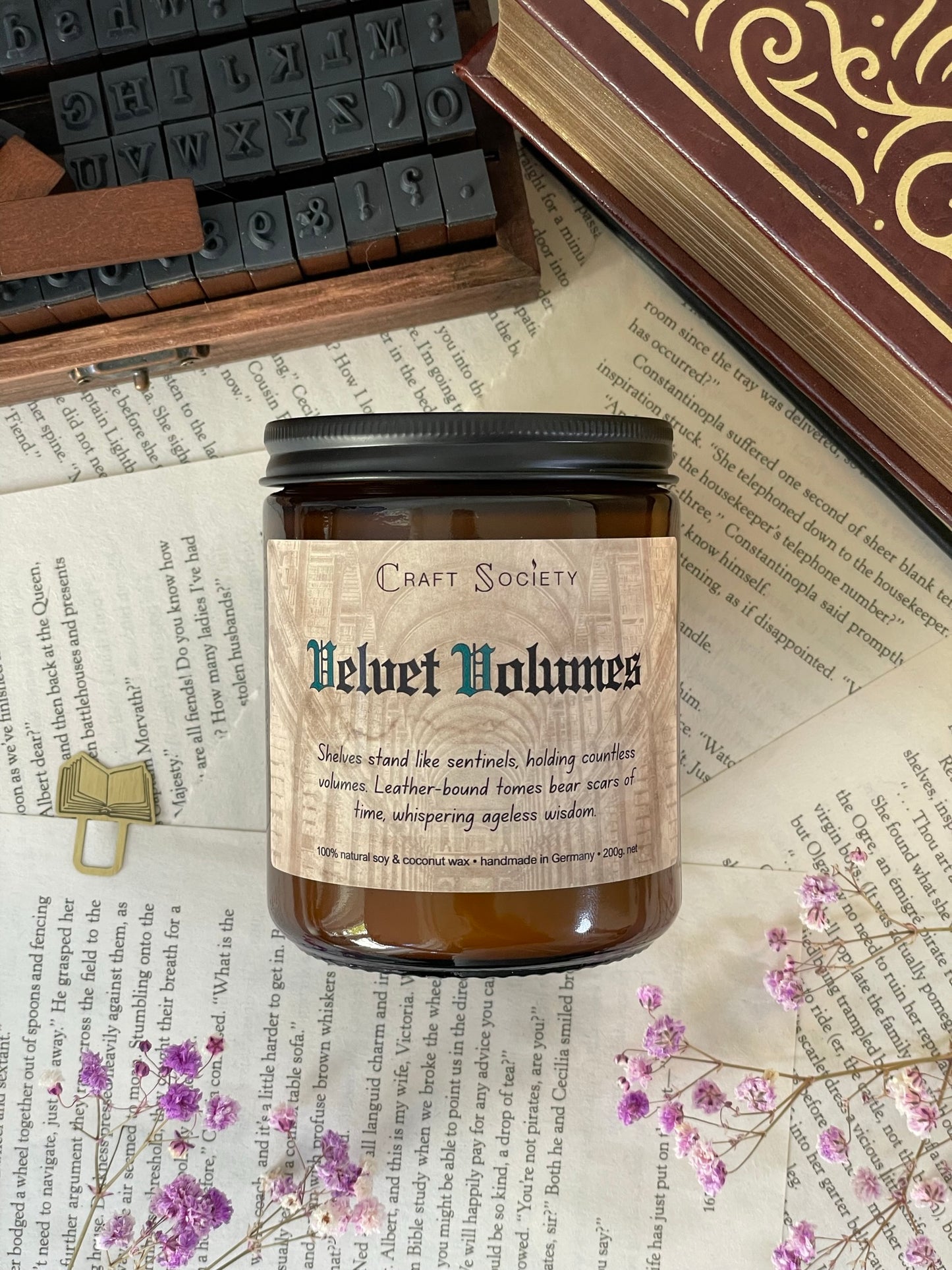 The Velvet Volumes scented candle in an amber jar from above on a dark academia background