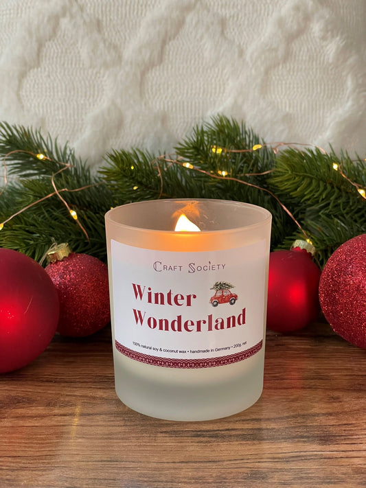 A burning deluxe scented candle in a frosted jar on a red holiday decorated background