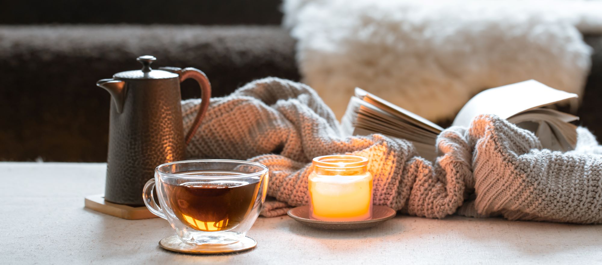 A cozy atmosphere showing a book, tea, and a lit scented candle