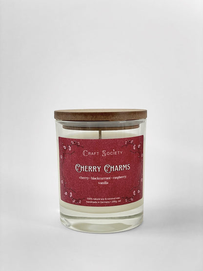 A scented candle called Cherry Charms on a white background, box, clear glass jar, regular version with cotton wick
