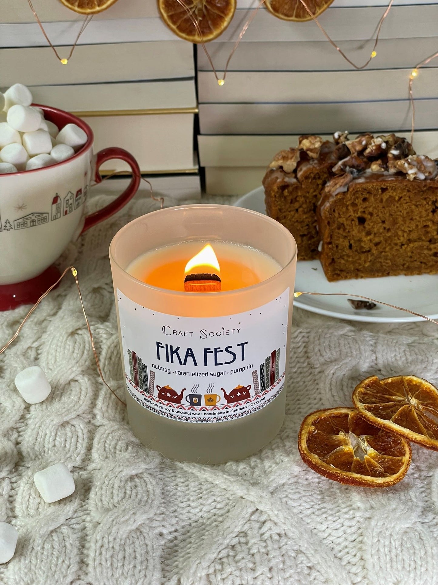 A burning deluxe scented candle made from vegetable wax on a decorated background with cake and marshmallows