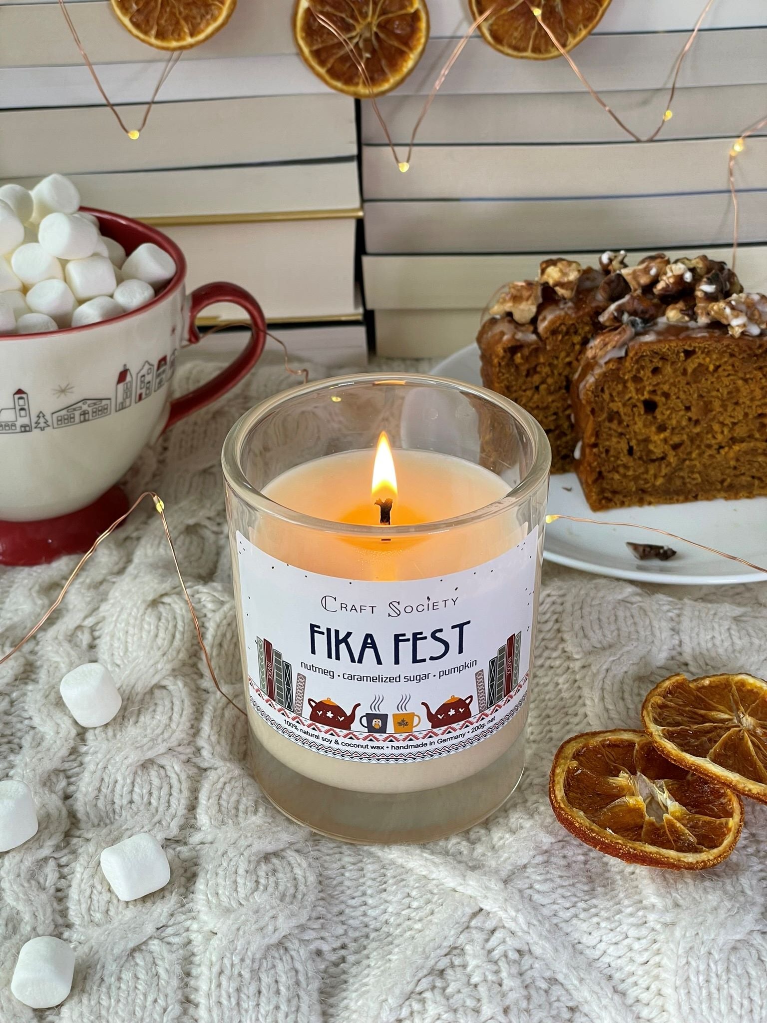 A burning scented candle made from vegetable wax on a decorated background with cake and marshmallows