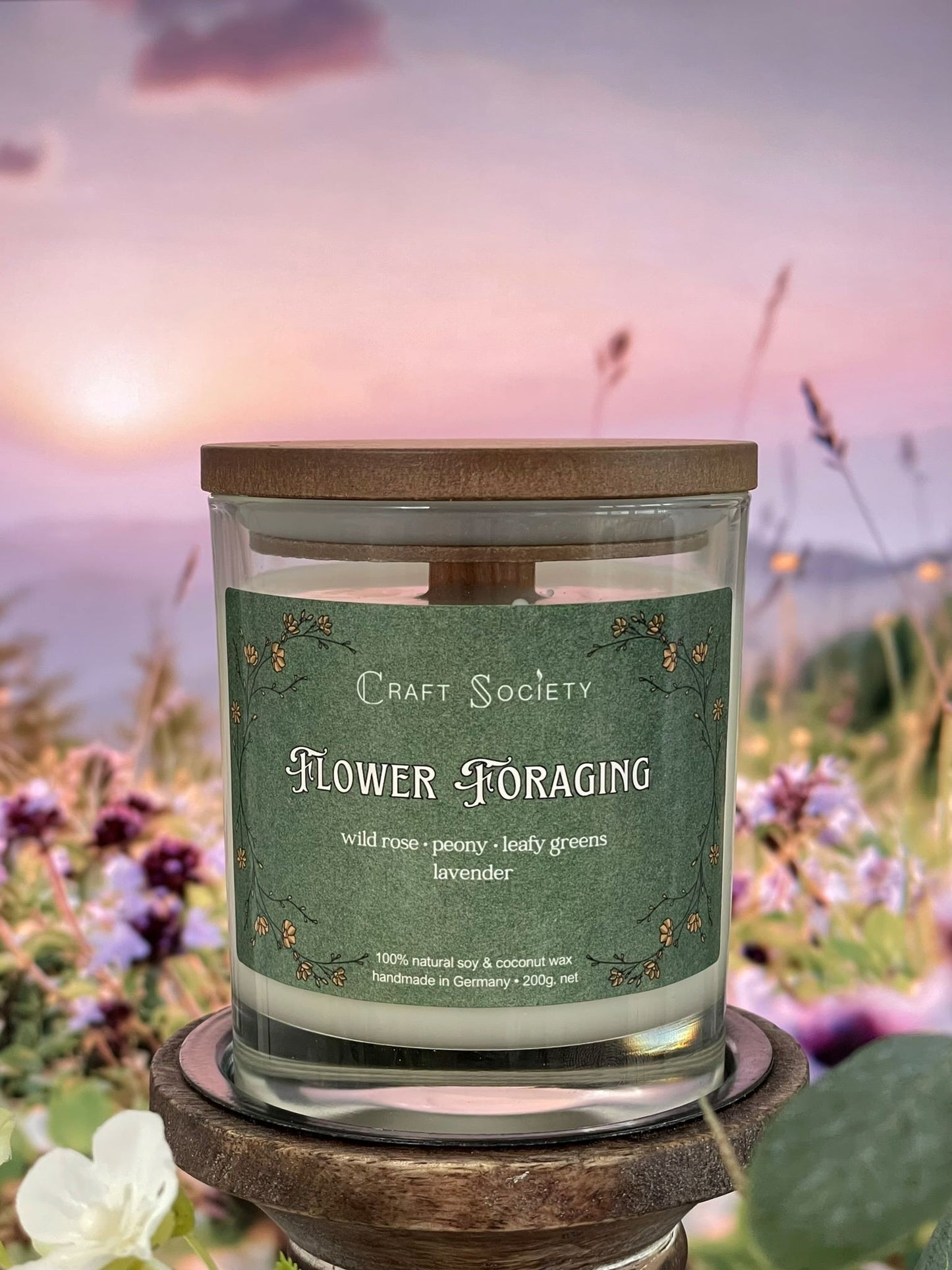 A scented candle called Flower Foraging on a floral and sunrise background, boxed, clear glass jar, deluxe version with wooden wick