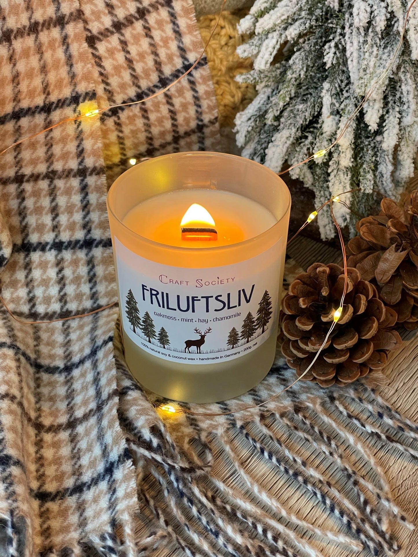 A burning deluxe scented candle on a decorated background with pine cones