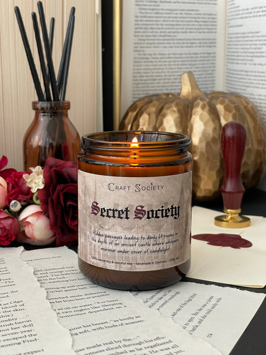 A burning scented candle, amber jar, on a dark academia decorated background