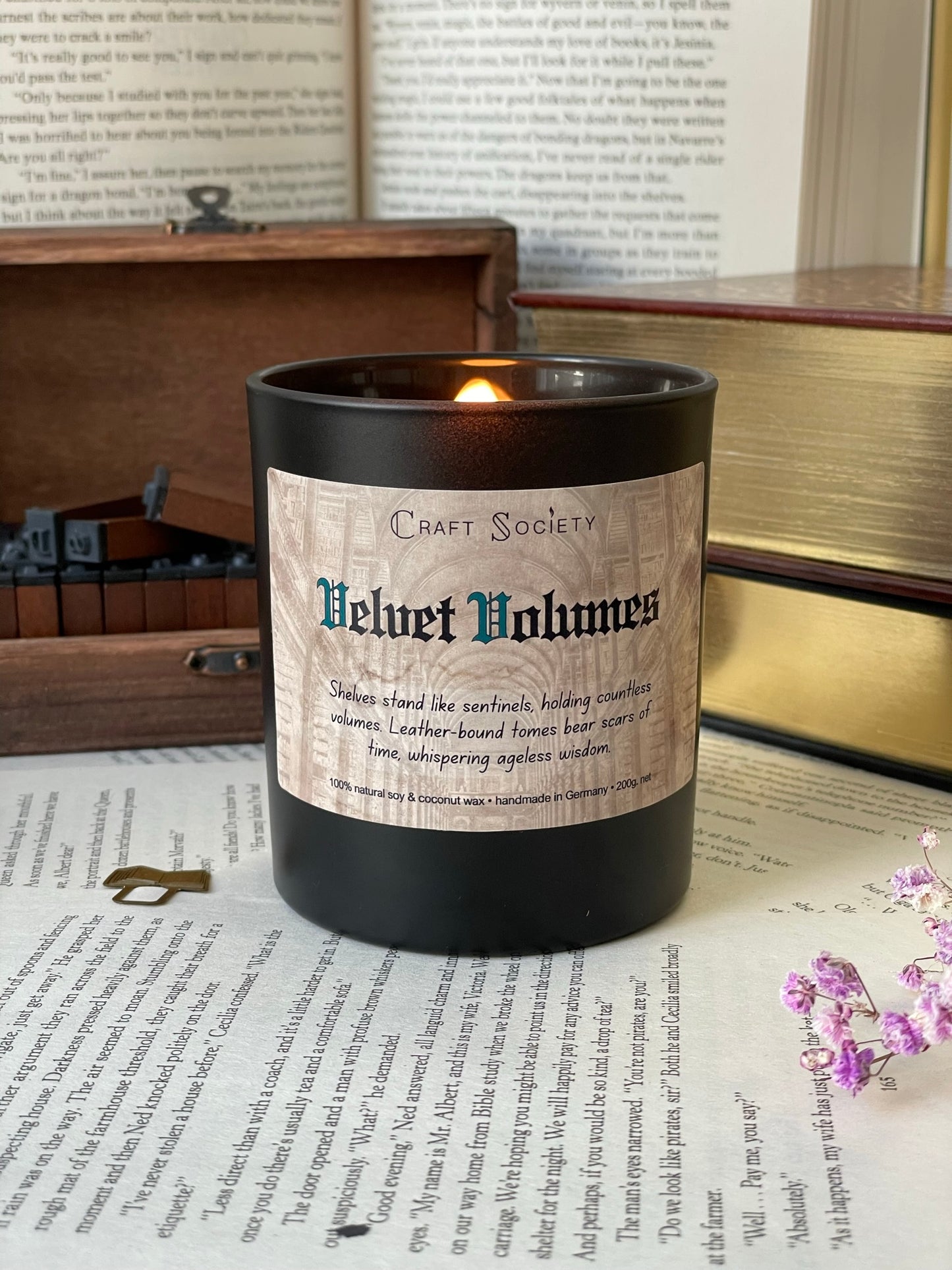 A burning deluxe scented candle in a black jar on a decorated background with books and texts