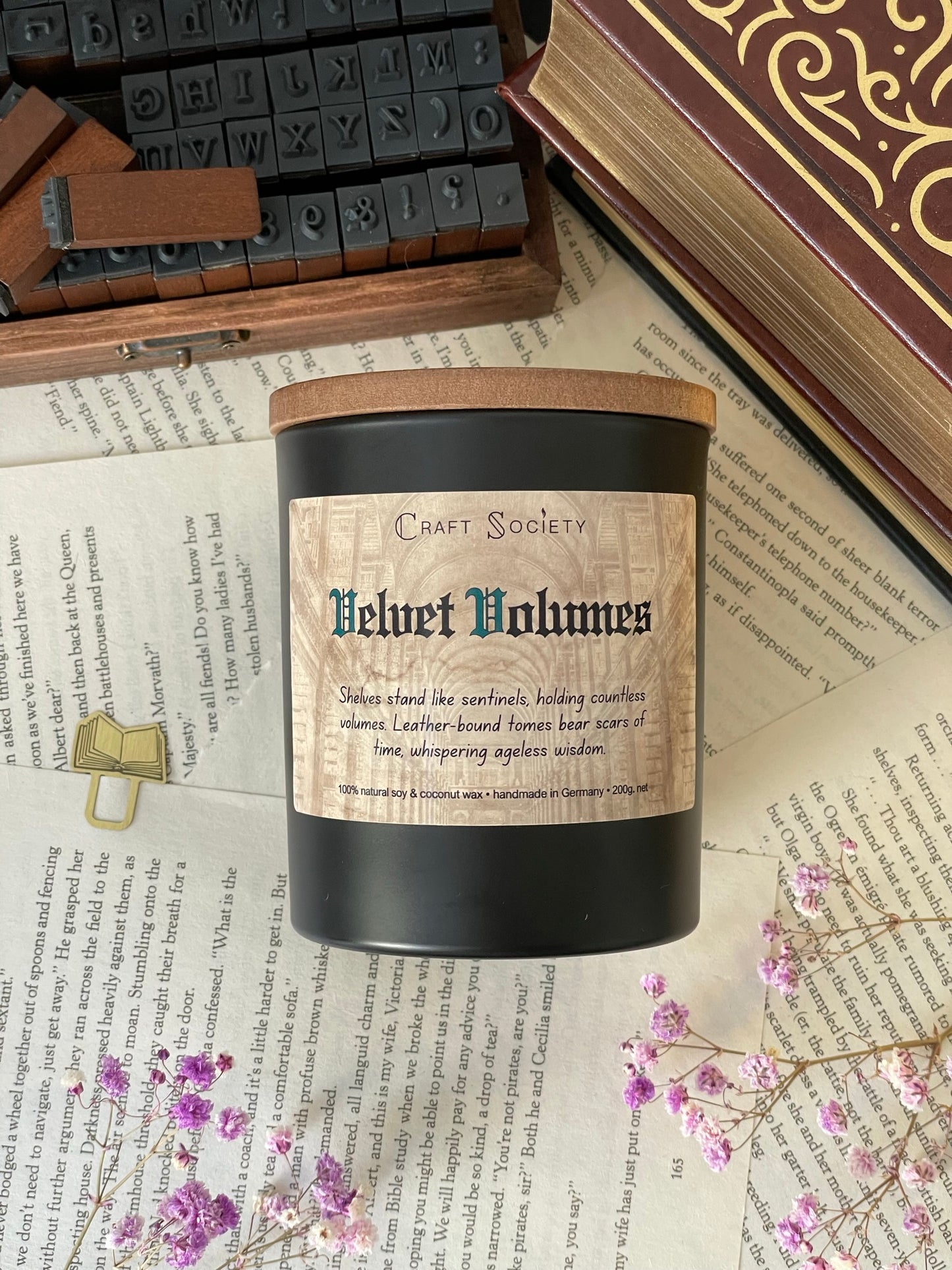 A deluxe scented candle in a black jar on a decorated background with books flowers and texts from above