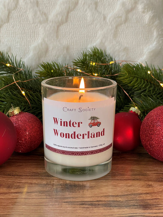 A burning scented candle in a clear jar on a red holiday decorated background