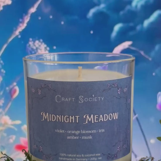 A scented candle called Midnight Meadow on a floral and night background, being lit, clear glass jar, regular version with cotton wick