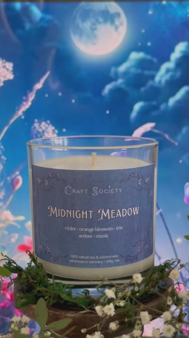 A scented candle called Midnight Meadow on a floral and night background, being lit, clear glass jar, regular version with cotton wick